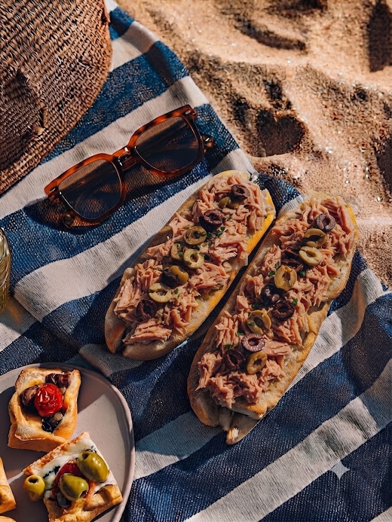 Dos bocadillos de atún y aceitunas sobre una toalla de playa.